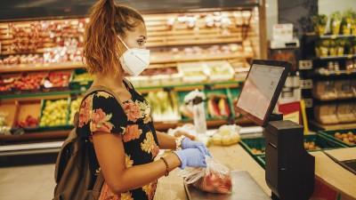  A woman wearing a face mask bags groceries at a checkout stand