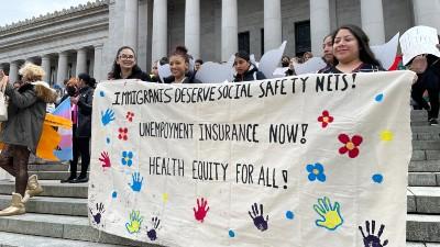 Activists hold a sign on the Washington State Capitol steps that reads "immigrants deserve social safety nets! Unemployment insurance now!"